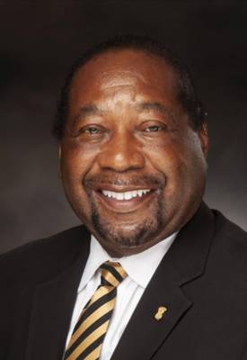 Smiling man in a suit with a striped tie, posed against a dark background.